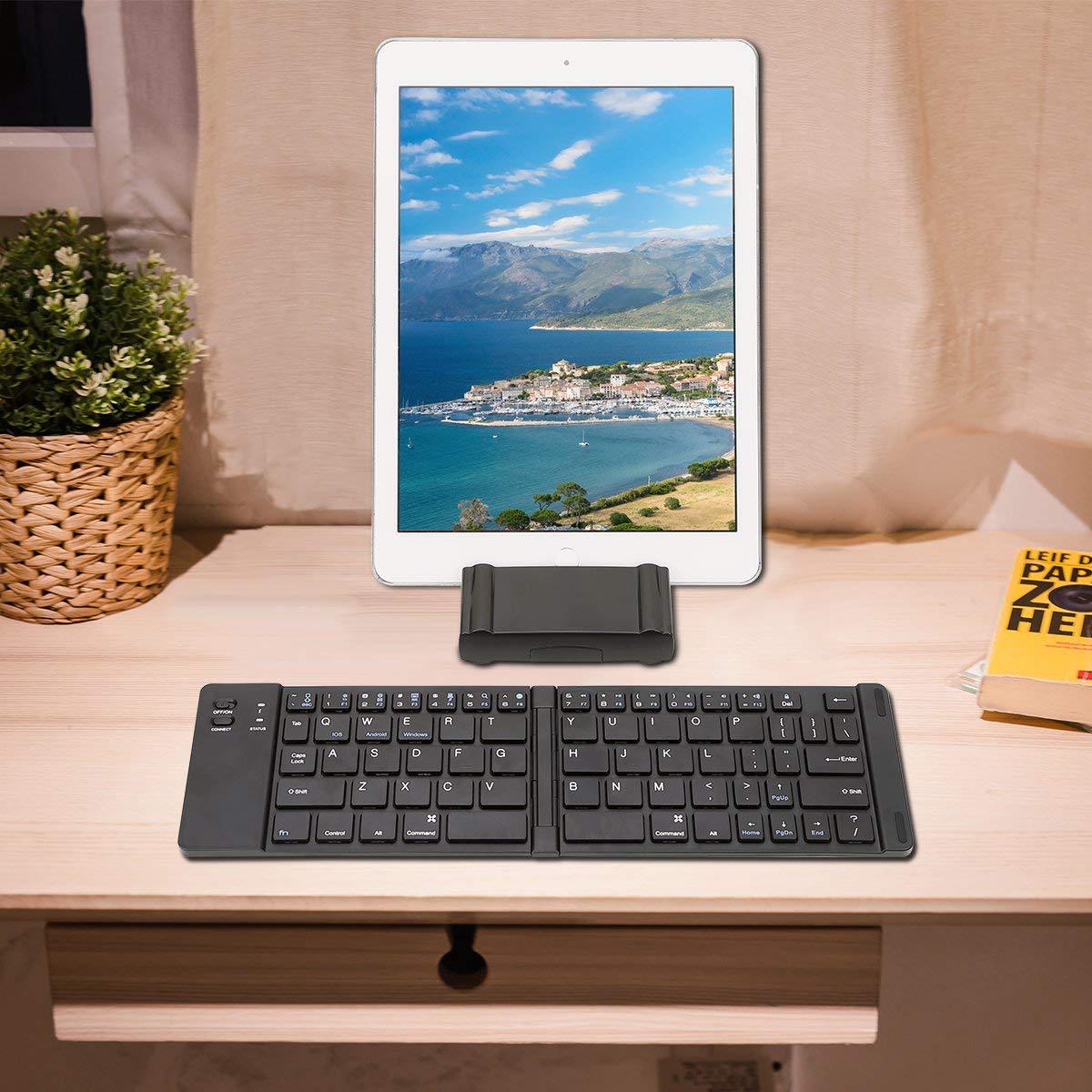 Tablet with a keyboard on a wooden surface next to a plant and book