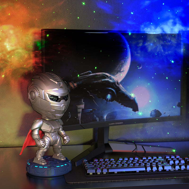 Silver superhero figurine with a red cape on a desk in front of a computer monitor displaying a space scene.